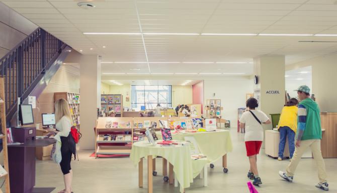 Espace central avec automates de prêt, tables de présentations et vue sur les collections