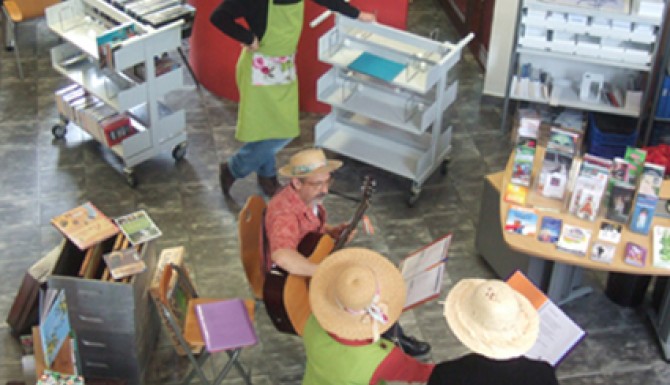 Animation jardins à Acigné. Des personnes habillées avec des tabliers de jardinage et des chapeaux de paille chantent et s'accompagnent à la guitare