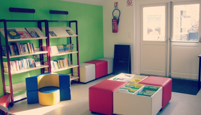 Entrée de la bibliothèque, avec les bacs et assises jeunesses. Le mur de gauche est vert