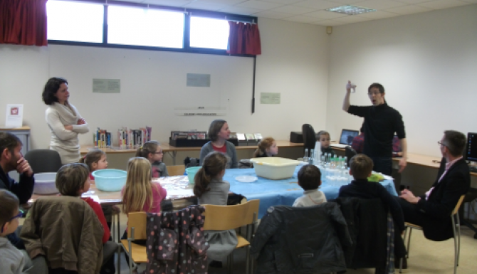 des enfants autour d'une grande table écoutent les instruction d'un animateur