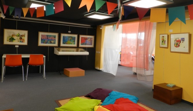 coin enfant très coloré avec des coussins colorés au sol, des chaises et des fanions accrochés au plafond