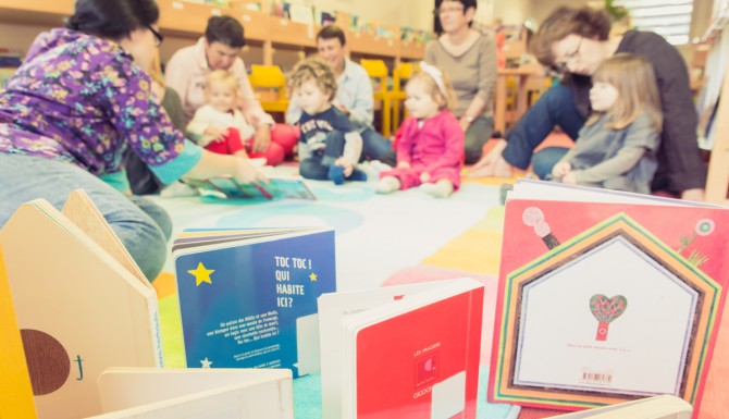 espace des enfants. Des livres jeunesse en premier plan et des adultes et leurs enfants en second plan