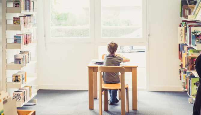 coin jeunesse. Un enfant lit assis sur une petite chaise/table. Des mangas sont aperçus à gauche et des albums à droite