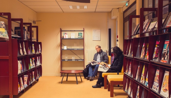 Presse et romans dans des rayonnages, personnes assise lisant des documents