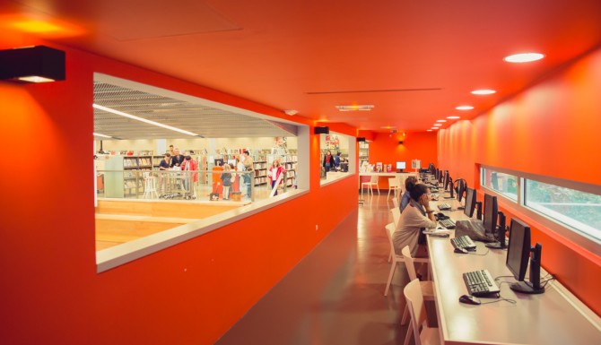 espace multimédia le long d'un couloir orange, percé d'une grande baie vitrée