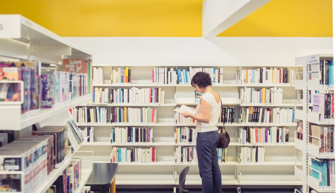 espace romans, des rayonnages blancs, un mur jaune et une personne feuilletant un livre