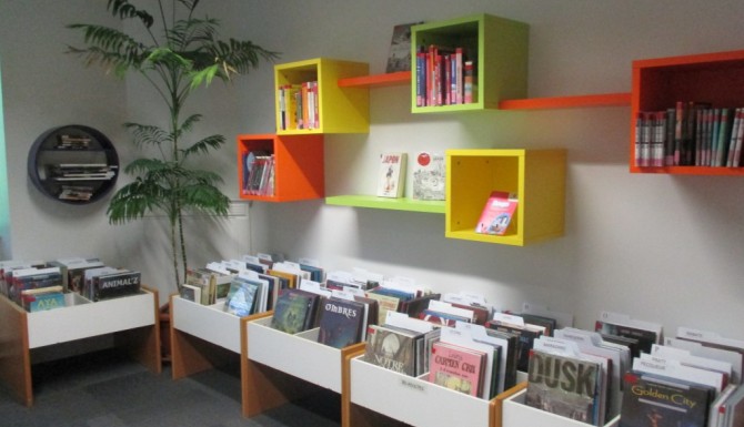 bandes dessinées dans des bacs bas. Des étagères fixées au mur de couleurs vives servent de présentoirs