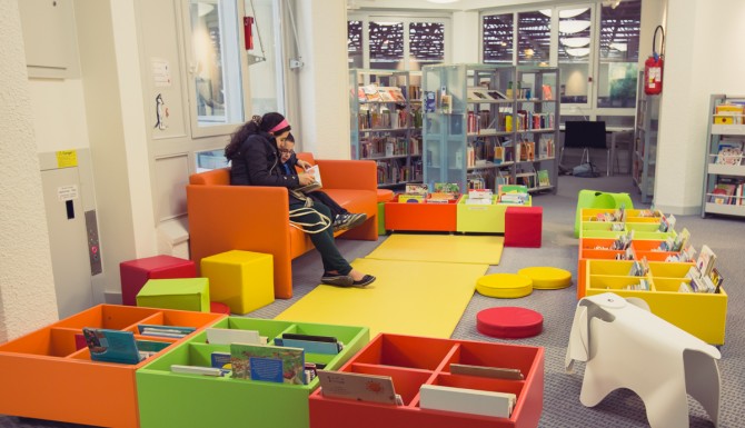 Espace enfants, très coloré. Banquette orange, tapis et bacs de toutes les couleurs. Un siège en forme d'éléphant