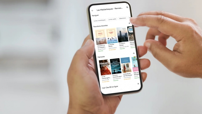 Mockup réalisé avec Smartmockup Zoom sur des mains tenant un smartphone. l'écran affiche la nouvelle application Aldiko