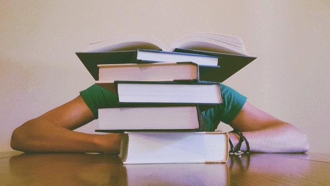CC0 Pixabay Un étudiant dormant sur son bureau dissimulé derrière une pile de livres.