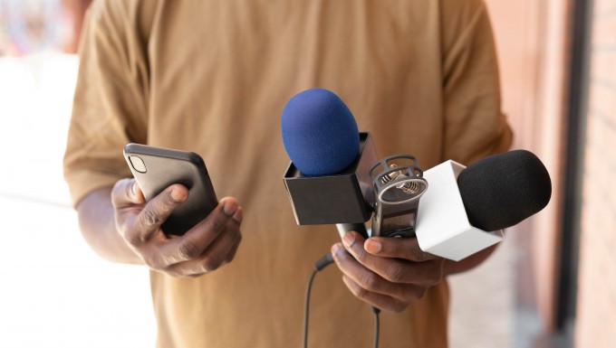 Chasseurs d'infos. Un homme tenant deux microphones et un enregistreur numérique.