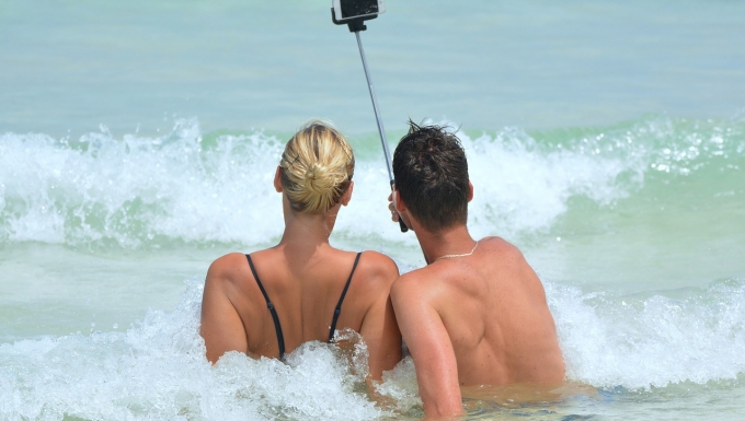 CC0 - Pixabay. Source : https://pixabay.com/fr/selfie-personnes-homme-femme-900001/) Un couple (vu de dos) prenant un selfie allongés dans les vagues.