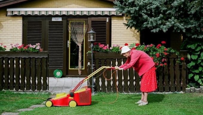 Photo © Klaus Pichler Graphisme © L’Atelier du Bourg grand mère habillée en fushia poussant une tondeuse dans un pavillon