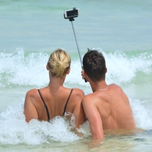 Un couple (vu de dos) prenant un selfie allongés dans les vagues.