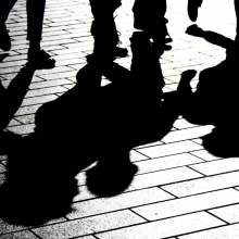 Photo en noir et blanc de personnes démabulant dont les ombres se reflétent au sol.