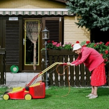 grand mère habillée en fushia poussant une tondeuse dans un pavillon